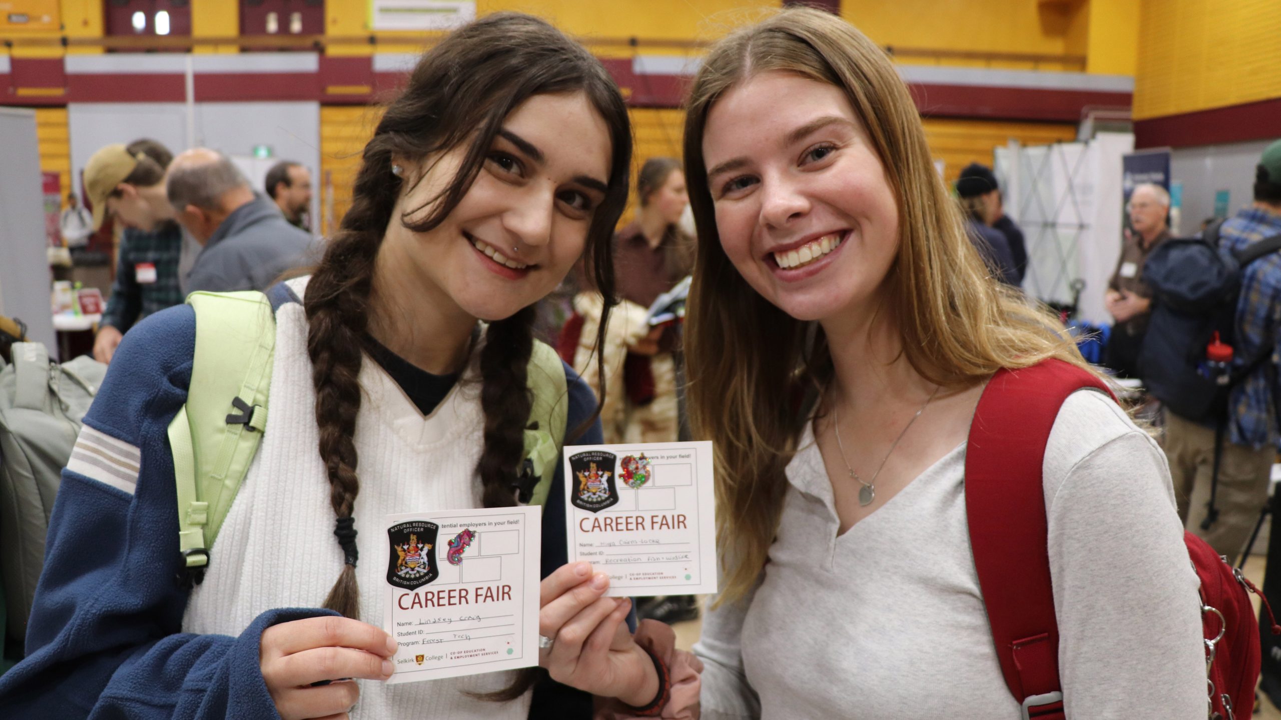 Two women standing holding College ID cards
