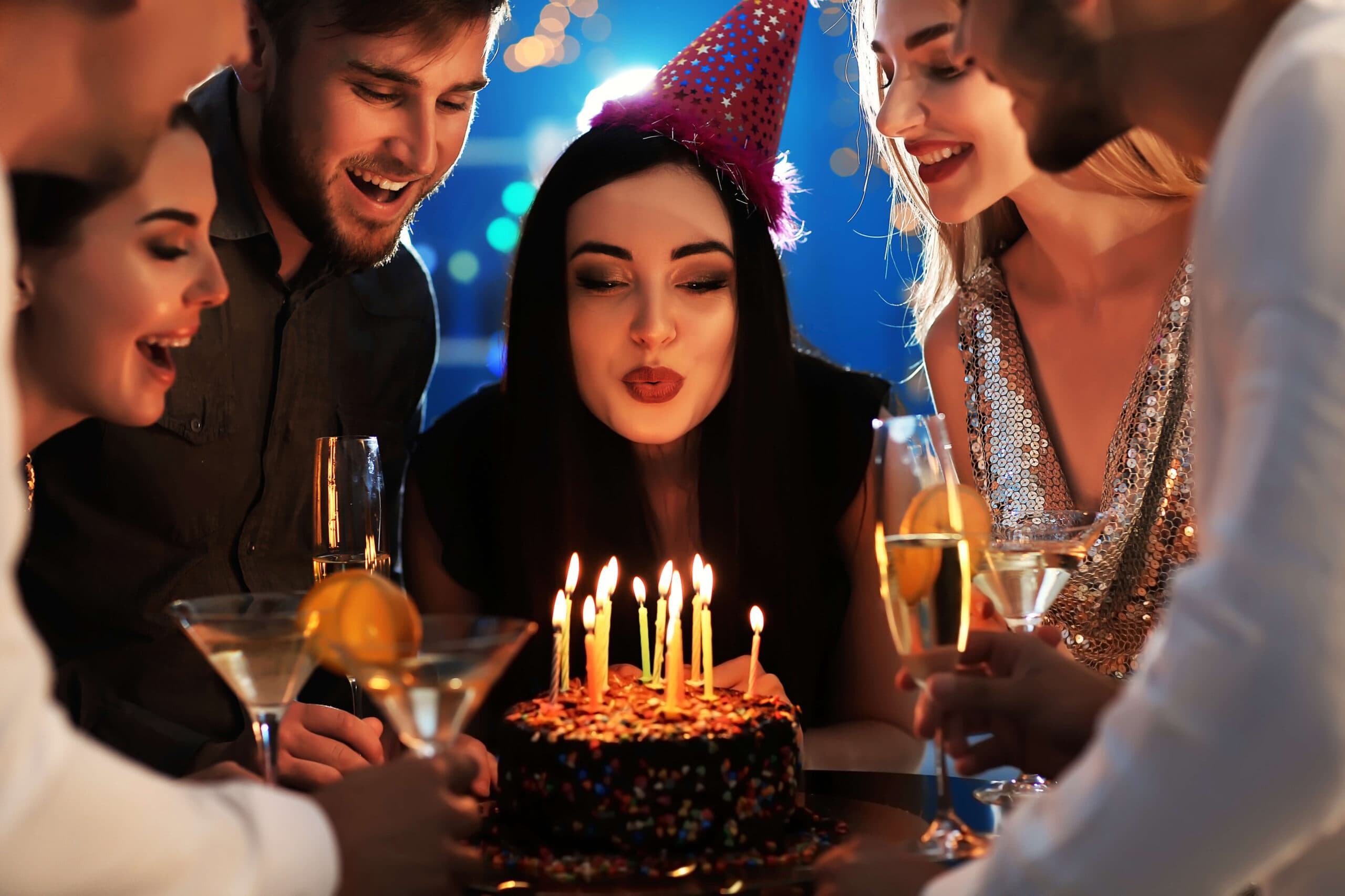 Woman blowing out birthday candles on a cake while celebrating with friends.
