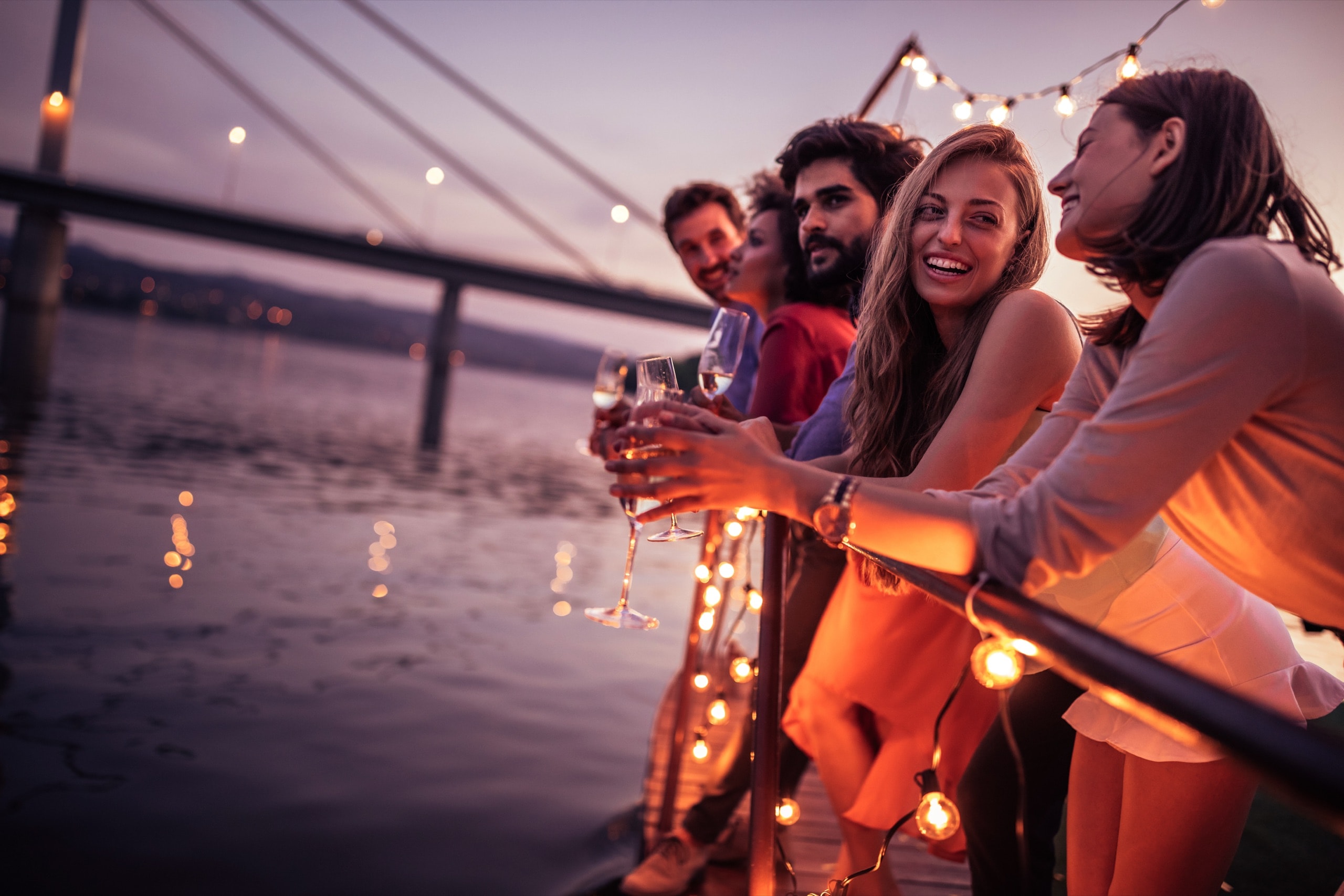 Colleagues toasting at sunset on a boat deck strung with lights during a corporate event cruise.